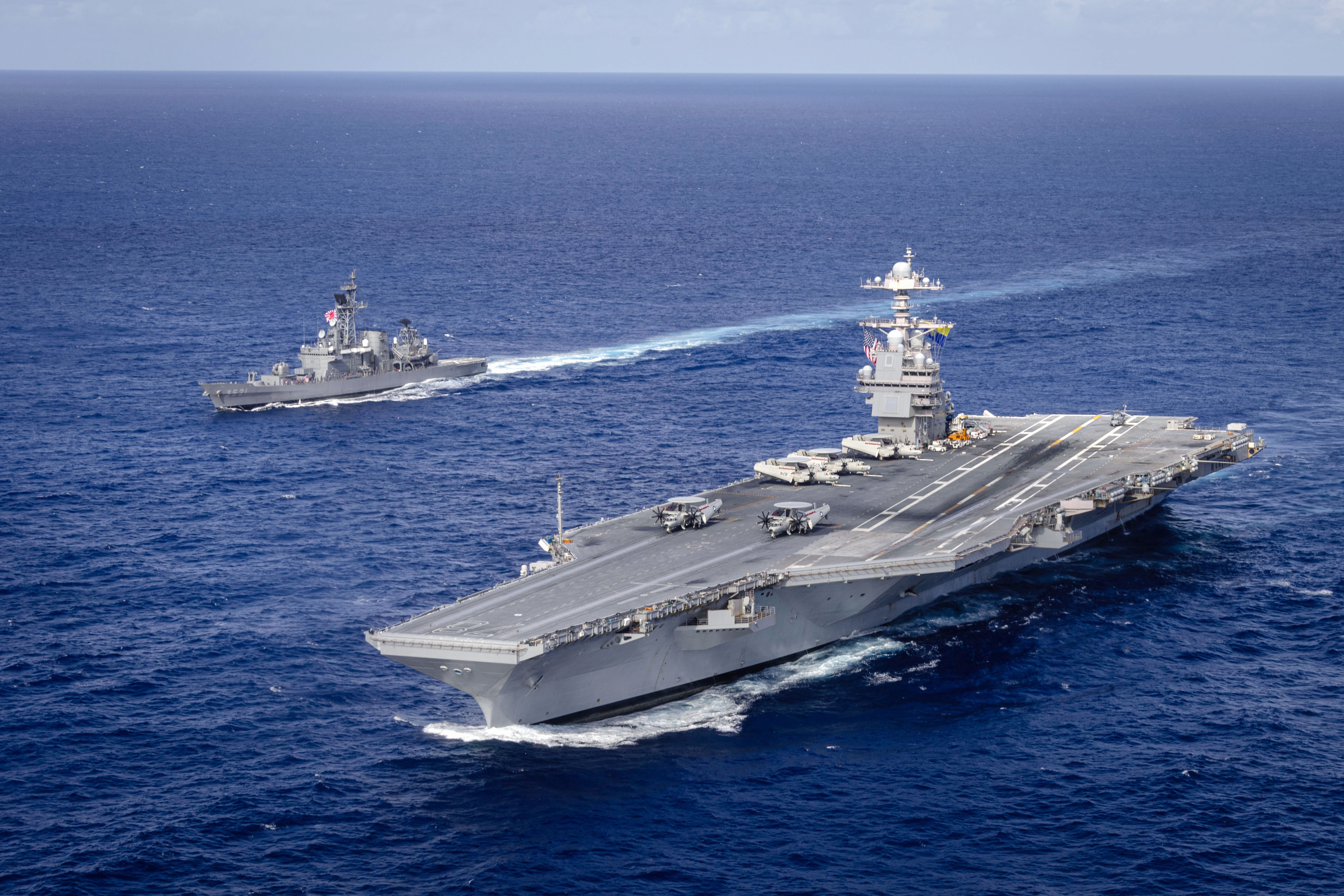 image of a large aircraft carrier moving in the ocean next to a smaller ship